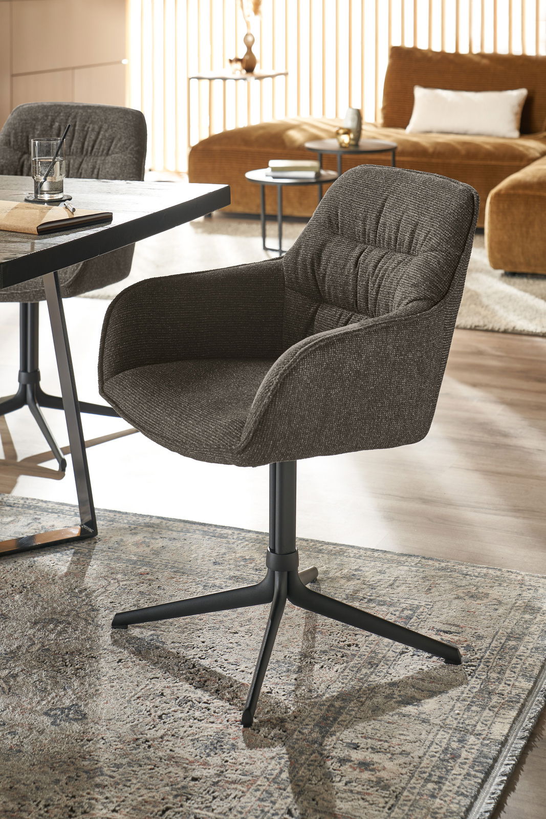 Moderner Armlehnstuhl in dunklem Stoffbezug, seitliche Perspektive, auf einem Teppich in einem stilvoll eingerichteten Raum.