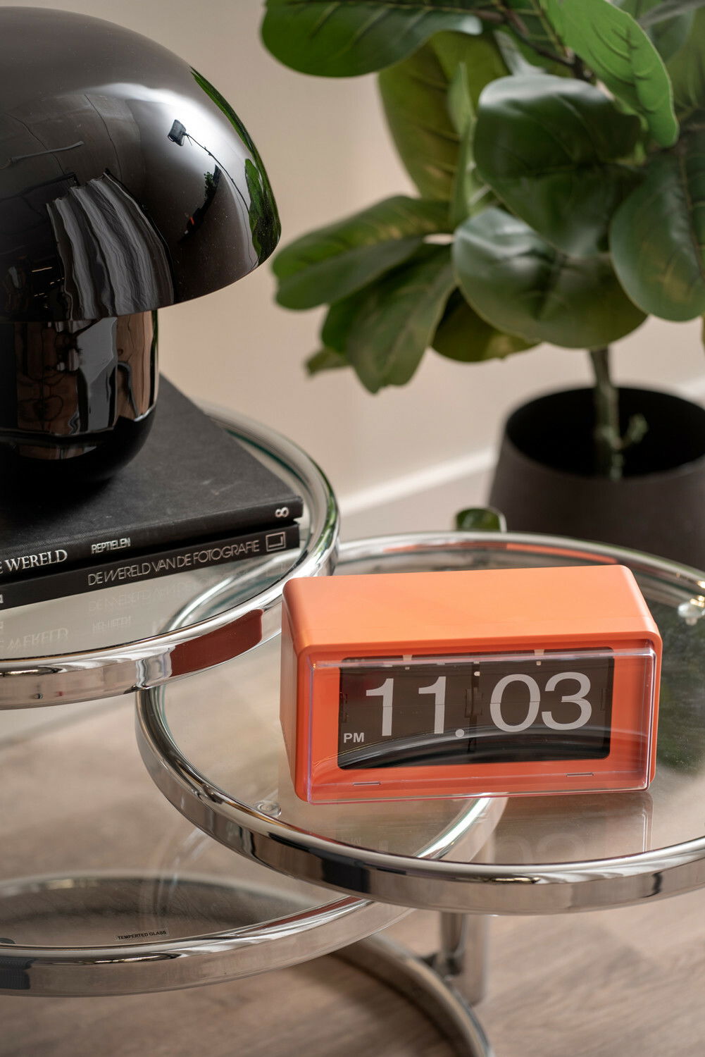 Orangefarbene Flip-Uhr auf einem gläsernen Beistelltisch, seitliche Perspektive.