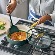 Person kocht Lachs in einer grünen Pfanne mit Glasdeckel auf einem Herd, seitliche Perspektive.