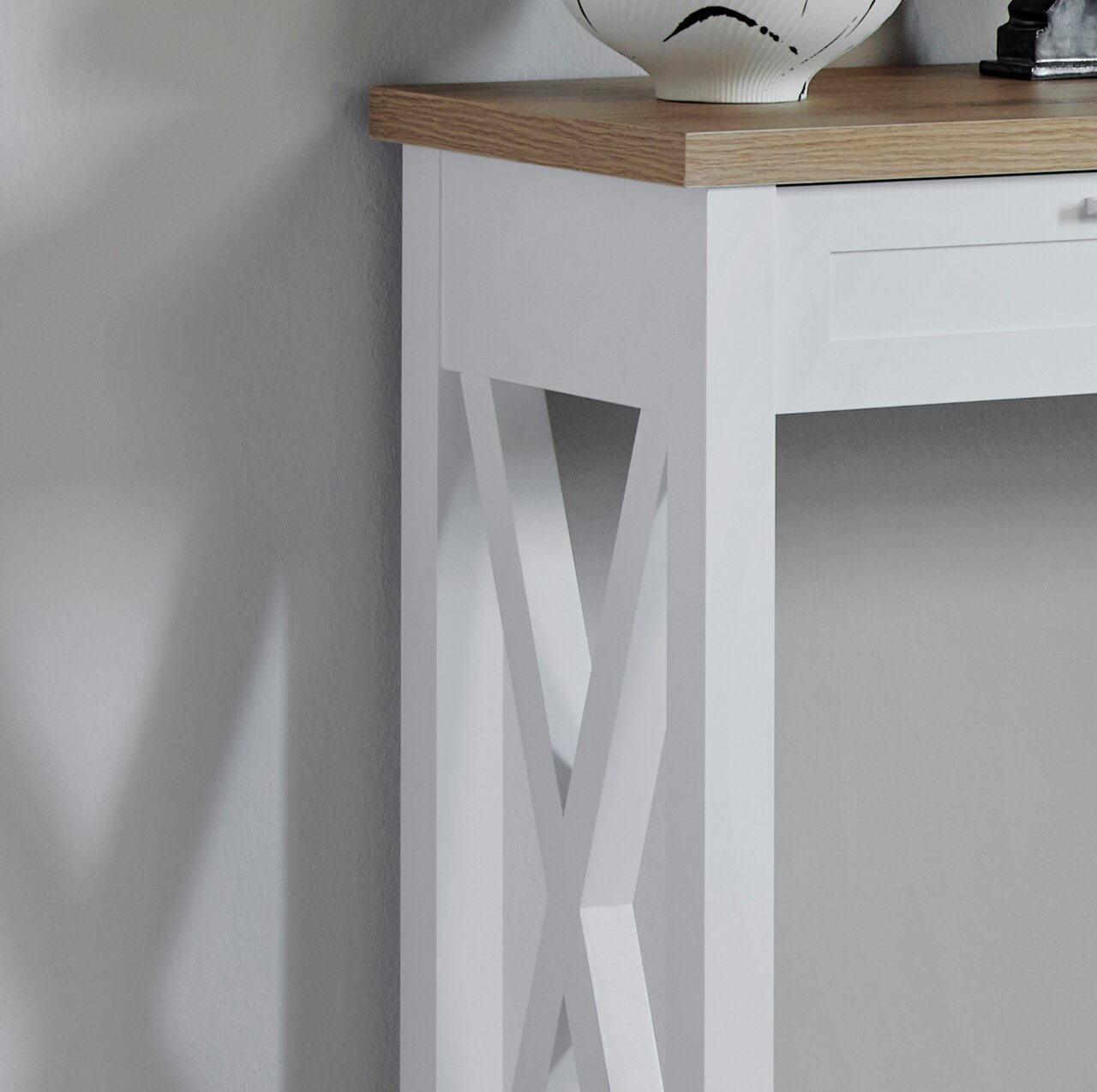 Detailfoto van een witte consoletafel met houten blad en een decoratief X-patroon aan de zijkant.