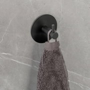 Schwarzer Wandhaken Uno Meleto an einer grauen Wand, von der Seite fotografiert, mit einem grauen Handtuch daran hängend.