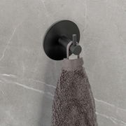 Schwarzer Wandhaken Uno Meleto an einer grauen Wand, von der Seite fotografiert, mit einem grauen Handtuch daran hängend.
