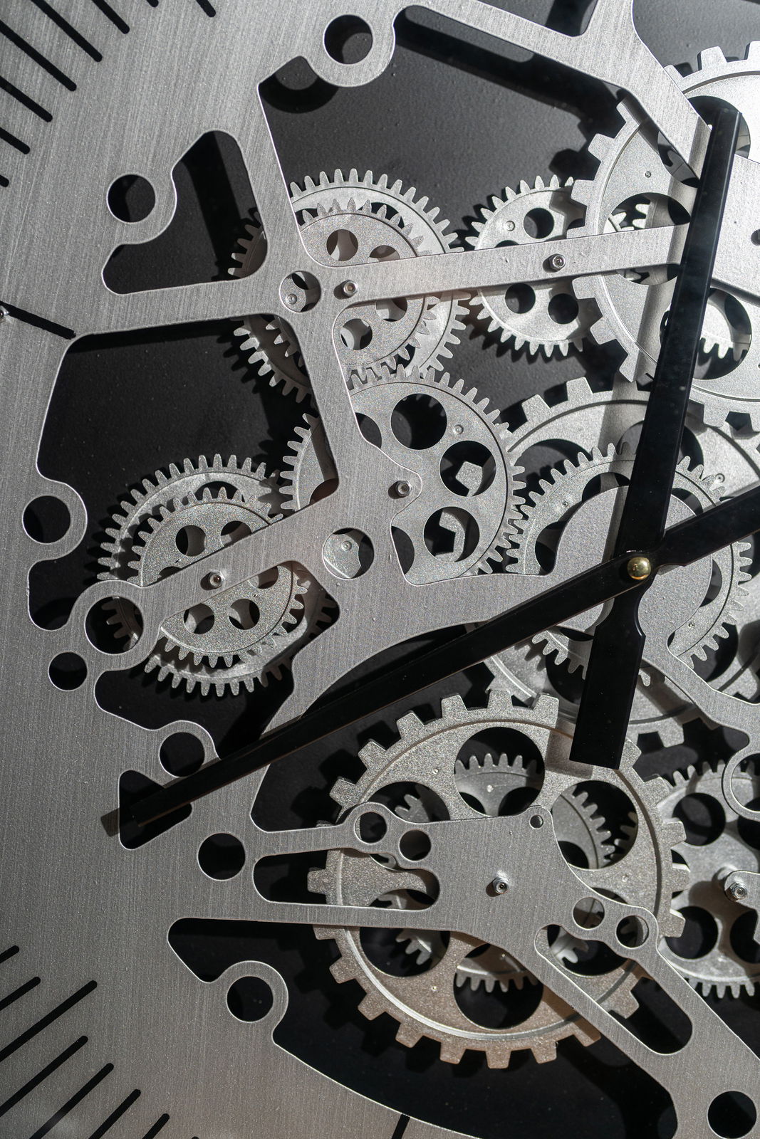 BHP Wanduhr Nahaufnahme einer silberfarbenen Wanduhr aus Metall mit sichtbaren Zahnrädern und schwarzen Zeigern, von vorne betrachtet.