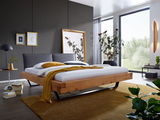 Modernes Balkenbett aus Holz mit schwarzem Kopfteil, seitliche Perspektive, in einem stilvoll eingerichteten Schlafzimmer mit großen Fenstern und Pflanzen.