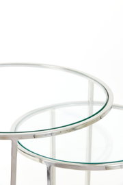 Close-up van twee ronde bijzettafels met glazen bladen en een zilverkleurig metalen frame, gefotografeerd vanuit een perspectief van bovenaf.
