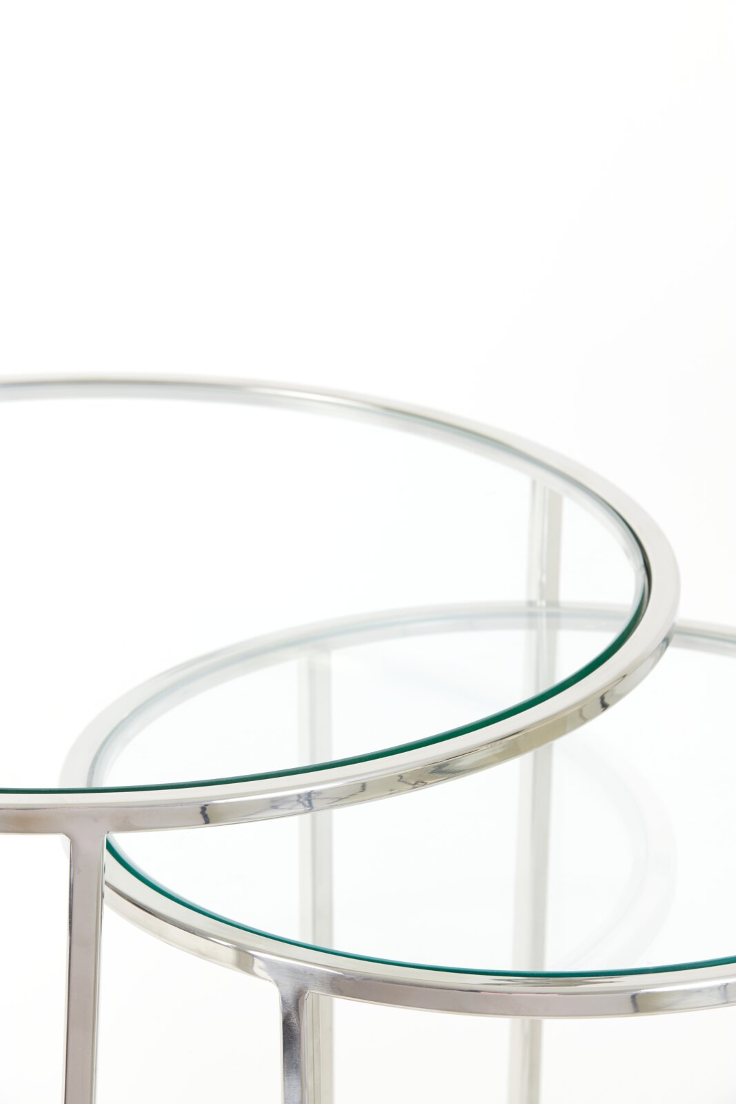 Close-up van twee ronde bijzettafels met glazen bladen en een zilverkleurig metalen frame, gefotografeerd vanuit een perspectief van bovenaf.