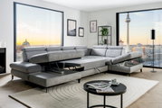 Graue Rundecke mit verstellbaren Kopfstützen und ausziehbarer Liegefläche in einem modernen Wohnzimmer mit Blick auf die Stadt. Perspektive von vorne links.