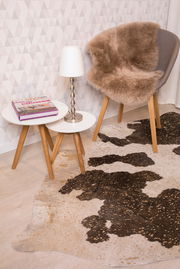 Schaffell auf einem Stuhl in einem modernen Raum mit Teppich und Beistelltischen, seitliche Perspektive