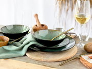Schwarz-grünes Keramikgeschirr-Set mit Schalen und Tellern auf Holztisch, mit goldenem Besteck und Weinglas, aufgenommen in schräger Seitenansicht von vorne.
