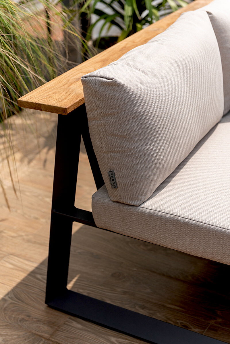 Nahaufnahme einer modernen Sitzbank mit Holzarmlehne und beigem Kissen, seitliche Perspektive.