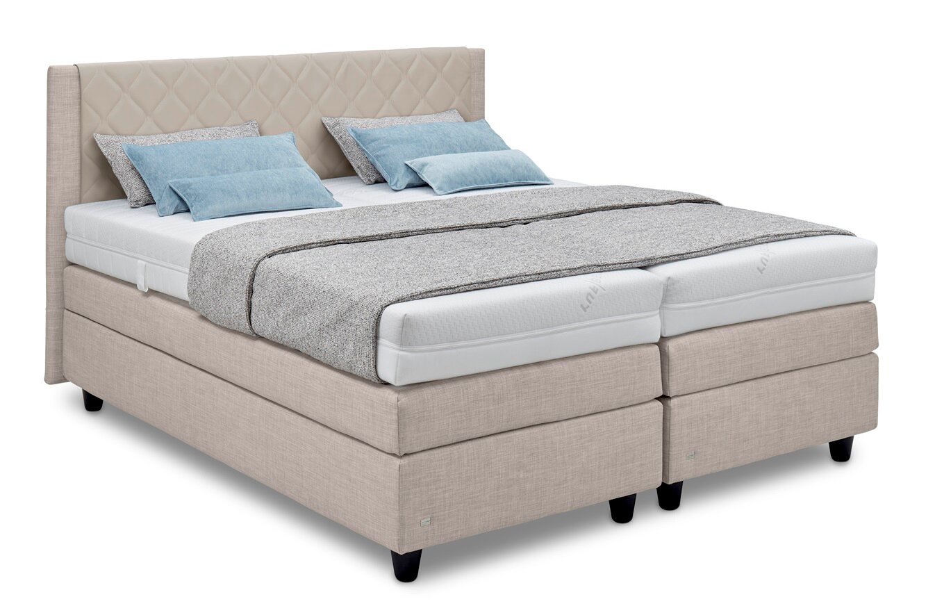 Boxspringbed in beige met doorgestikt hoofdeinde, grijze deken en blauwe kussens, zijaanzicht