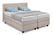 Boxspringbed in beige met doorgestikt hoofdeinde, grijze deken en blauwe kussens, zijaanzicht
