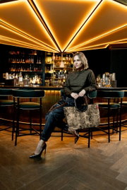 Een vrouw zit in een stijlvolle bar en houdt een grote tas met een patroon en ronde handvatten vast. De tas is van voren te zien.