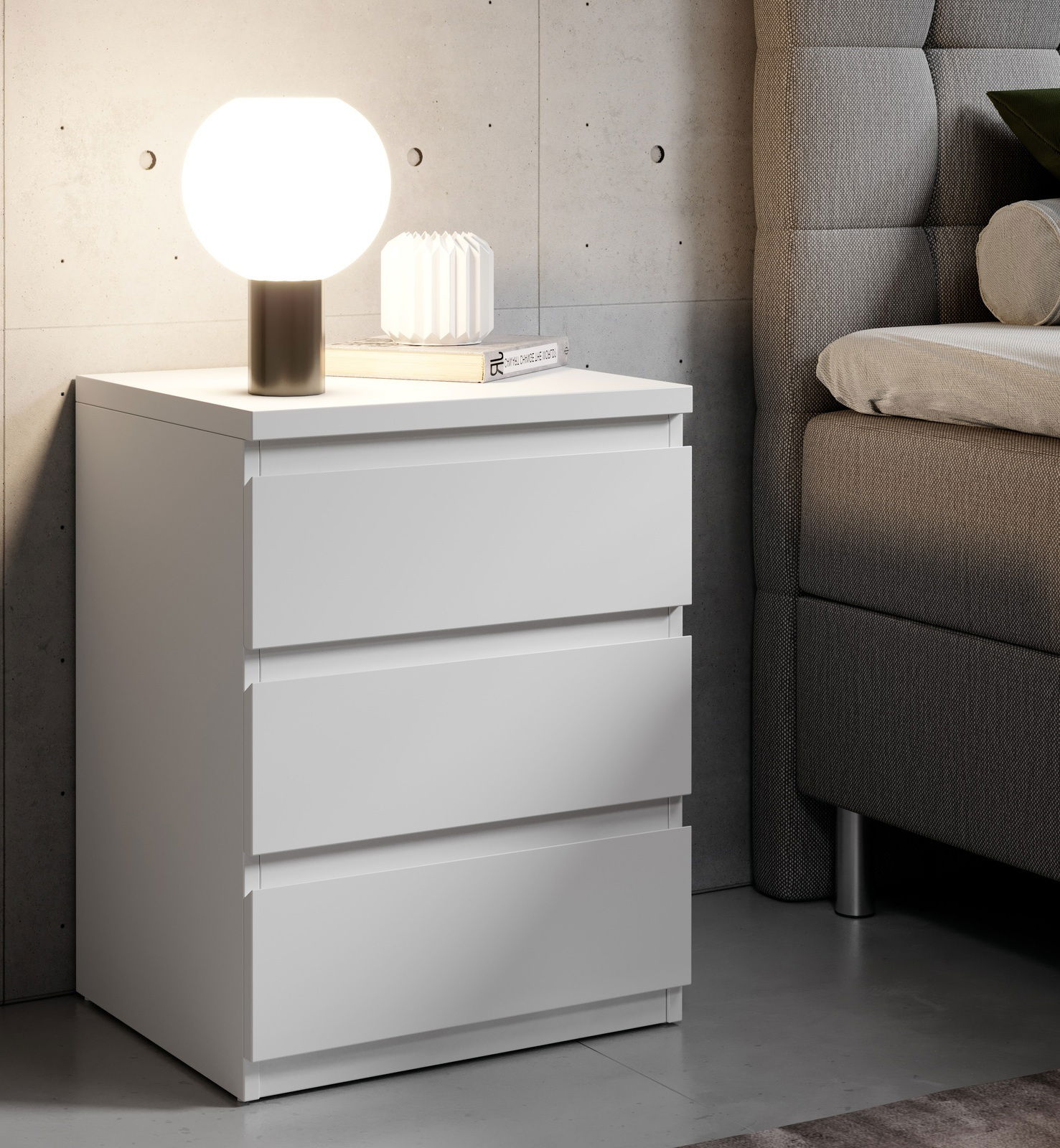 Weiße Nachtkommode mit drei Schubladen, darauf eine runde Lampe und ein Buch, seitliche Perspektive