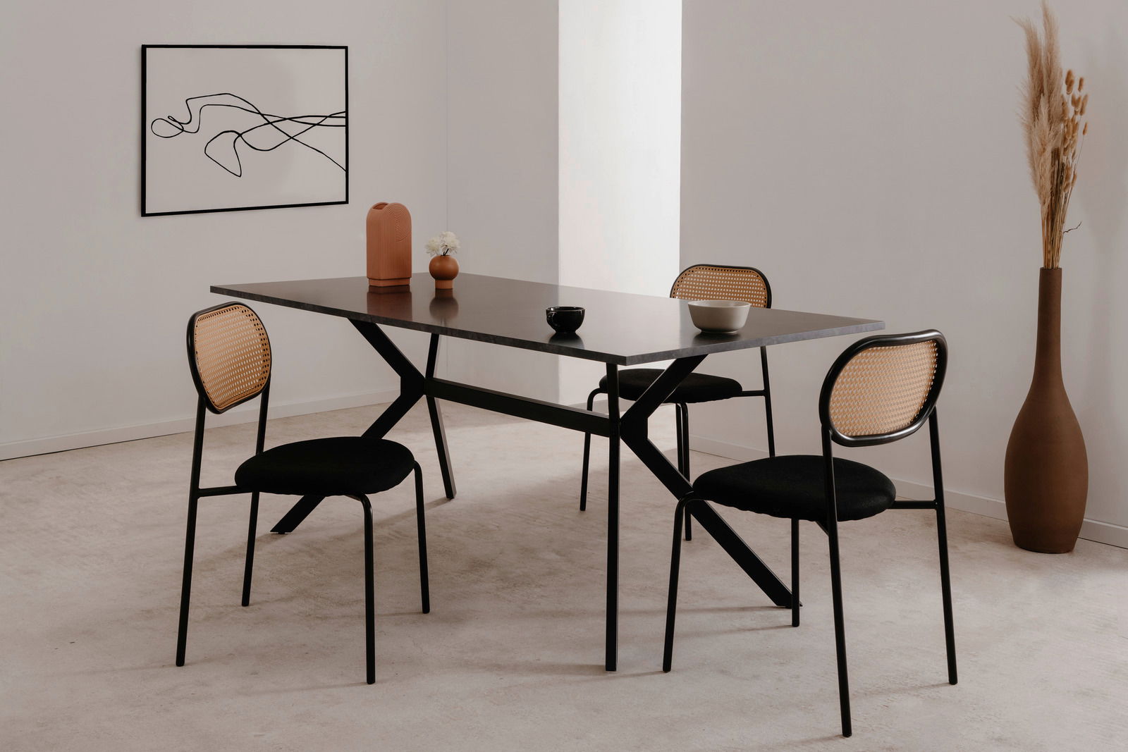 Moderner Esstisch mit schwarzer Tischplatte und schwarzen Stühlen mit geflochtenen Rückenlehnen, seitliche Perspektive.