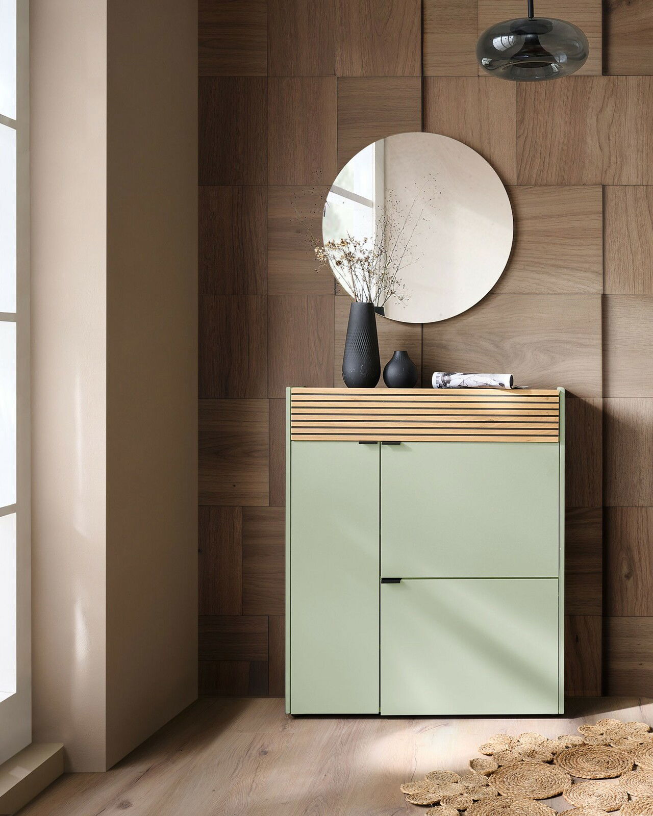 Garderoben-Set in Taupegrün mit modernem Design, bestehend aus einem Schrank mit Holzdetails und einem runden Spiegel, seitliche Perspektive.