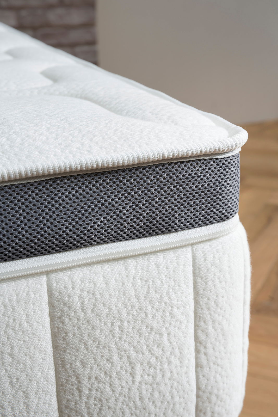 Nahaufnahme einer Matratze mit weißem Bezug und grauem, atmungsaktivem Seitenstreifen, seitliche Perspektive