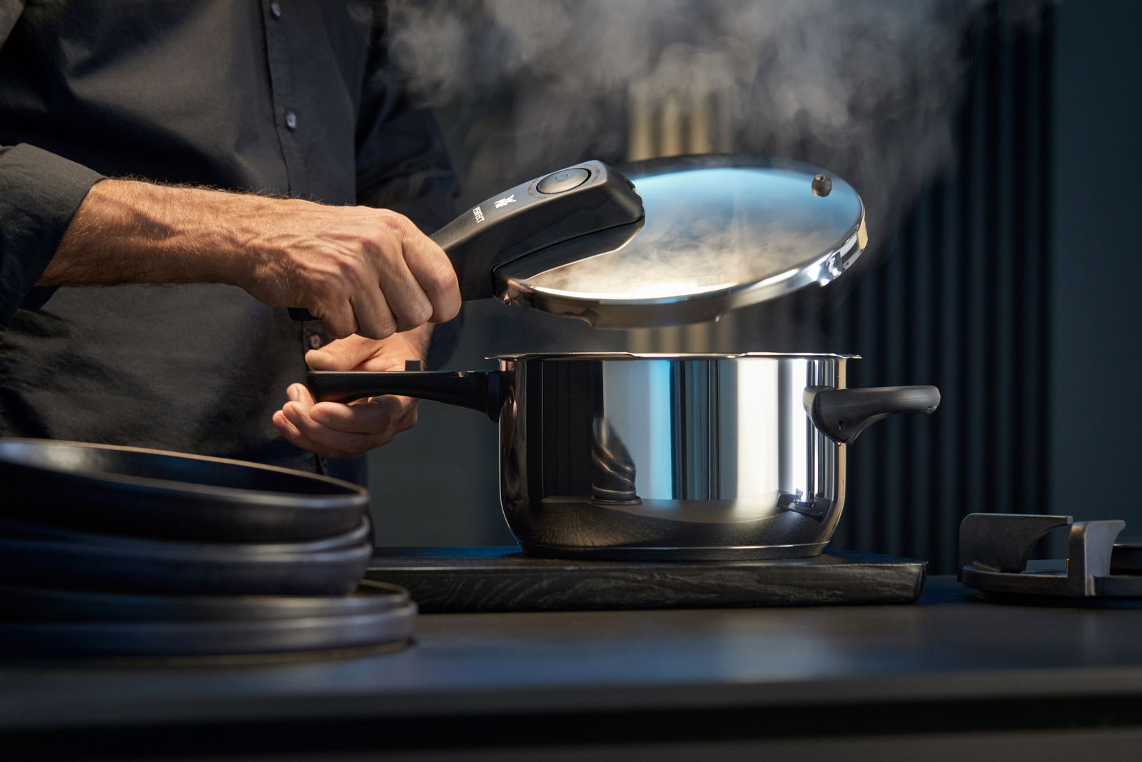 WMF Schnelltopf Set PERFECT NEU Mann öffnet einen dampfenden Schnellkochtopf aus Edelstahl in einer modernen Küche, seitliche Perspektive.