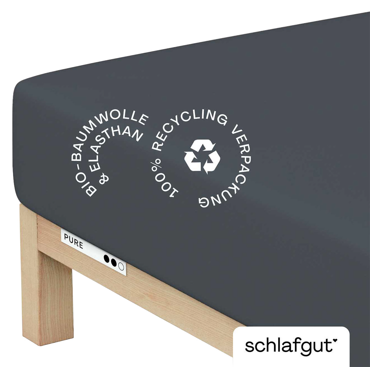 Spannbettlaken aus Bio-Baumwolle und Elasthan in dunkler Farbe, auf einer Matratze von der Seite fotografiert, mit Hinweis auf 100% Recycling-Verpackung.