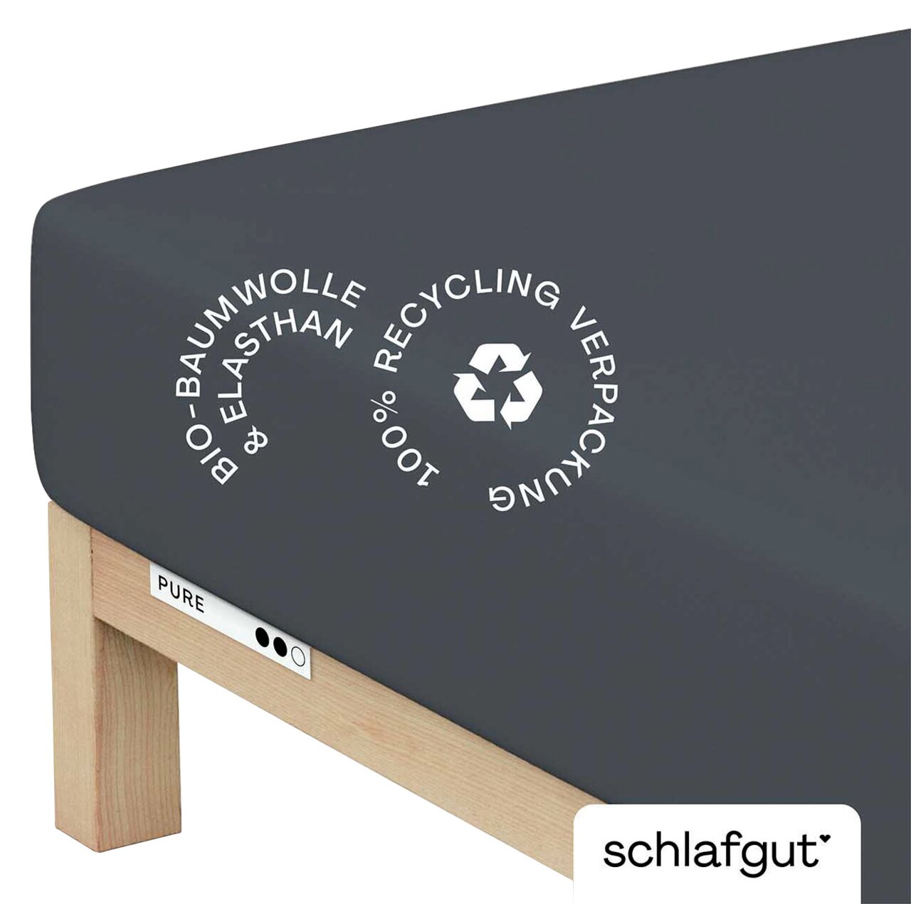 Spannbettlaken aus Bio-Baumwolle und Elasthan in dunkler Farbe, auf einer Matratze von der Seite fotografiert, mit Hinweis auf 100% Recycling-Verpackung.