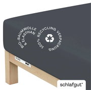 Spannbettlaken aus Bio-Baumwolle und Elasthan in dunkler Farbe, auf einer Matratze von der Seite fotografiert, mit Hinweis auf 100% Recycling-Verpackung.