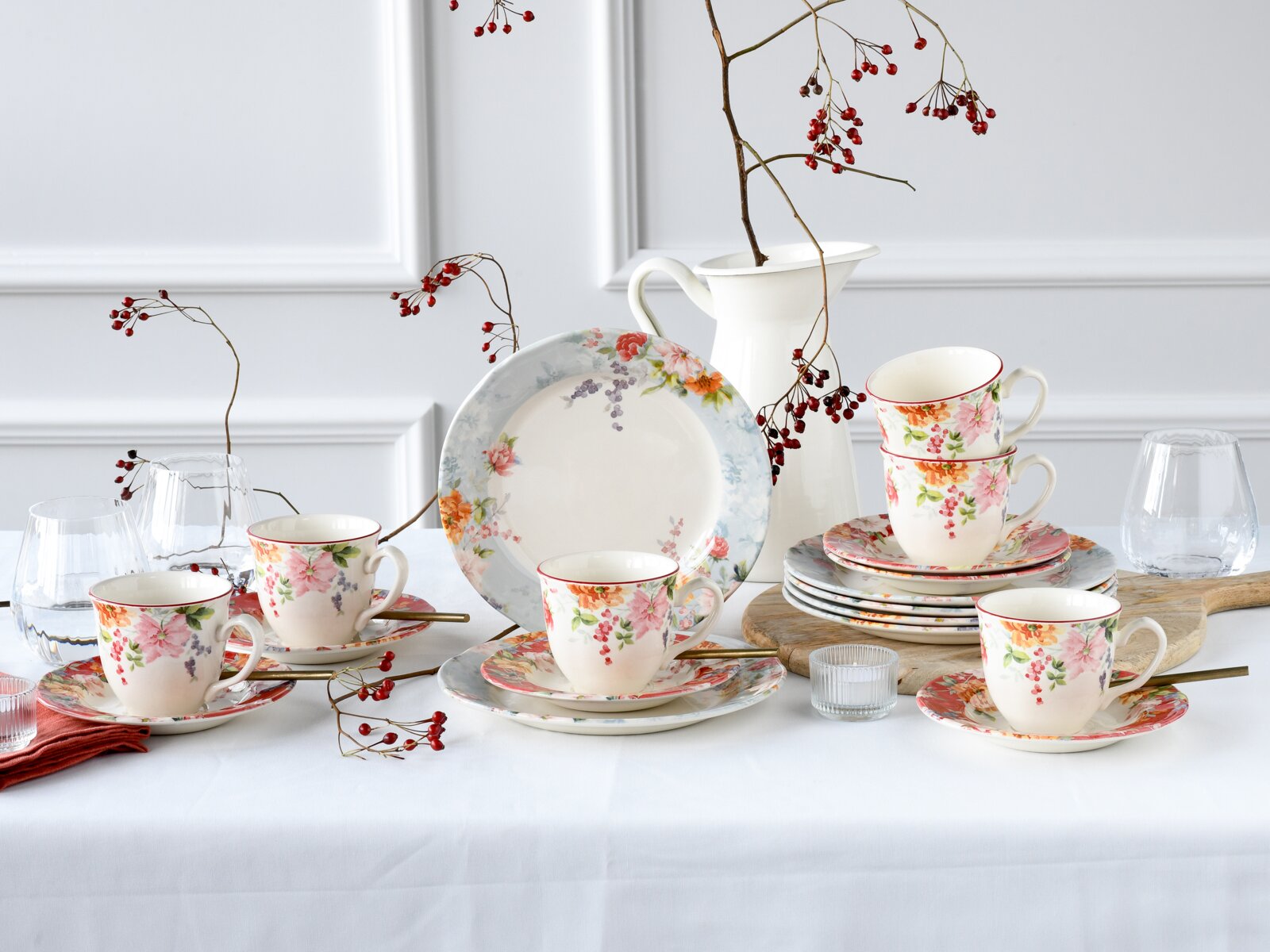 creaTable Kaffeeservice 18-tlg CRIMSON Florales Porzellan-Geschirrset mit Tassen, Untertassen und Tellern in Pastelltönen, dekoriert mit Blumenmotiven, arrangiert auf weiß gedecktem Tisch mit Krug, Gläsern und roten Beerenzweigen, frontal in leicht erhöhter Perspektive
