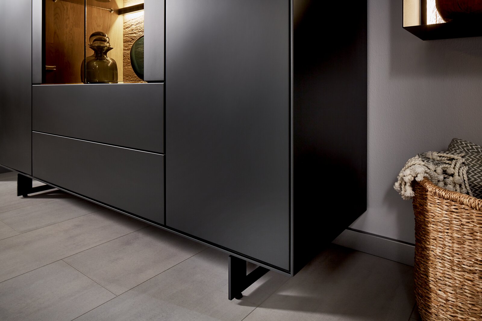 Nahaufnahme eines modernen, schwarzen Highboards mit Glasvitrine, seitliche Perspektive.