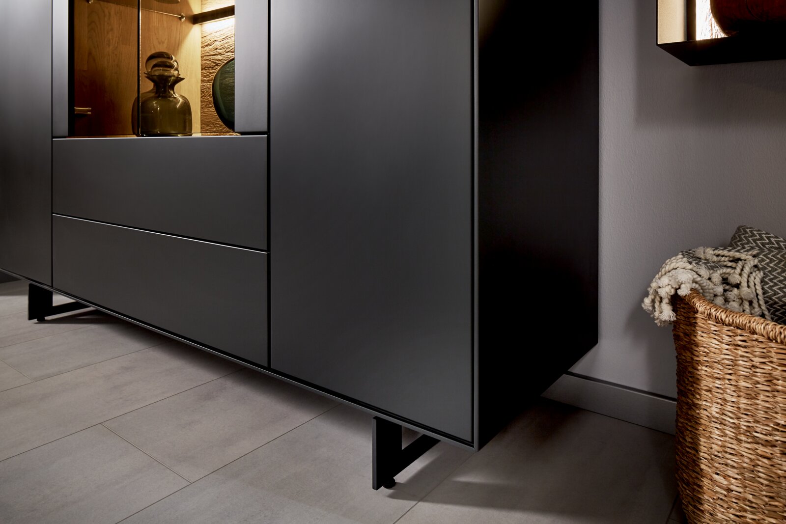 Nahaufnahme eines modernen, schwarzen Highboards mit Glasvitrine, seitliche Perspektive.