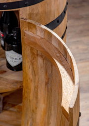 Nahaufnahme eines Bar-Fasses aus Holz mit schwarzen Metallringen, teilweise geöffnet, mit Flaschen im Inneren sichtbar. Perspektive von oben.