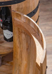 Nahaufnahme eines Bar-Fasses aus Holz mit schwarzen Metallringen, teilweise geöffnet, mit Flaschen im Inneren sichtbar. Perspektive von oben.