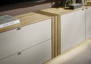 Modernes Lowboard/Sideboard mit hellgrauen Fronten und Holzplatte, mittig geriffeltem Holzelement und aufliegenden Büchern, in schräger Frontansicht von oben.