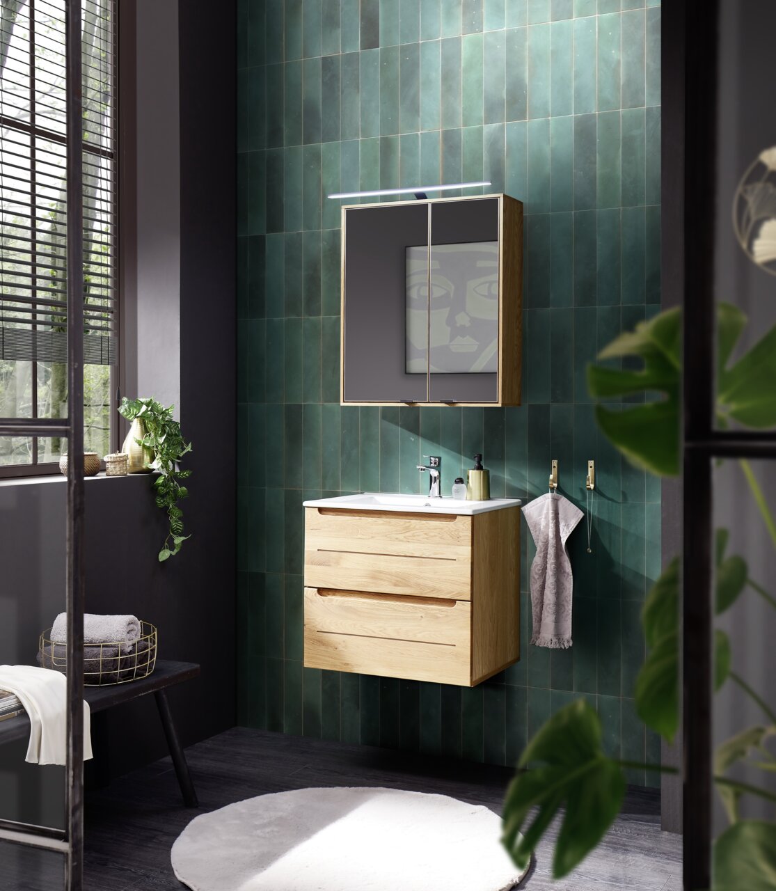 Moderne keramische wastafel met houten onderkast, gezien van voren in een stijlvol ingerichte badkamer met groene wandtegels en natuurlijk licht.