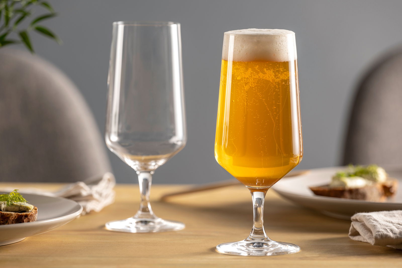 Leonardo Bierglas 6er-Set PUCCINI Zwei elegante Biergläser auf einem gedeckten Tisch, eines gefüllt mit sprudelndem Bier, aus seitlicher Perspektive fotografiert.
