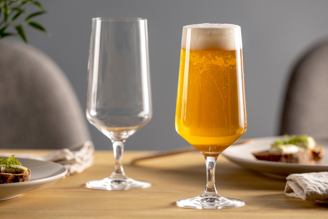 Twee elegante bierglazen op een gedekte tafel, waarvan één gevuld met bruisend bier, gefotografeerd vanuit een zijaanzicht.