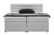 Frontale Ansicht eines grauen Boxspringbetts mit gepolstertem Kopfteil und schwarzem Kissen.