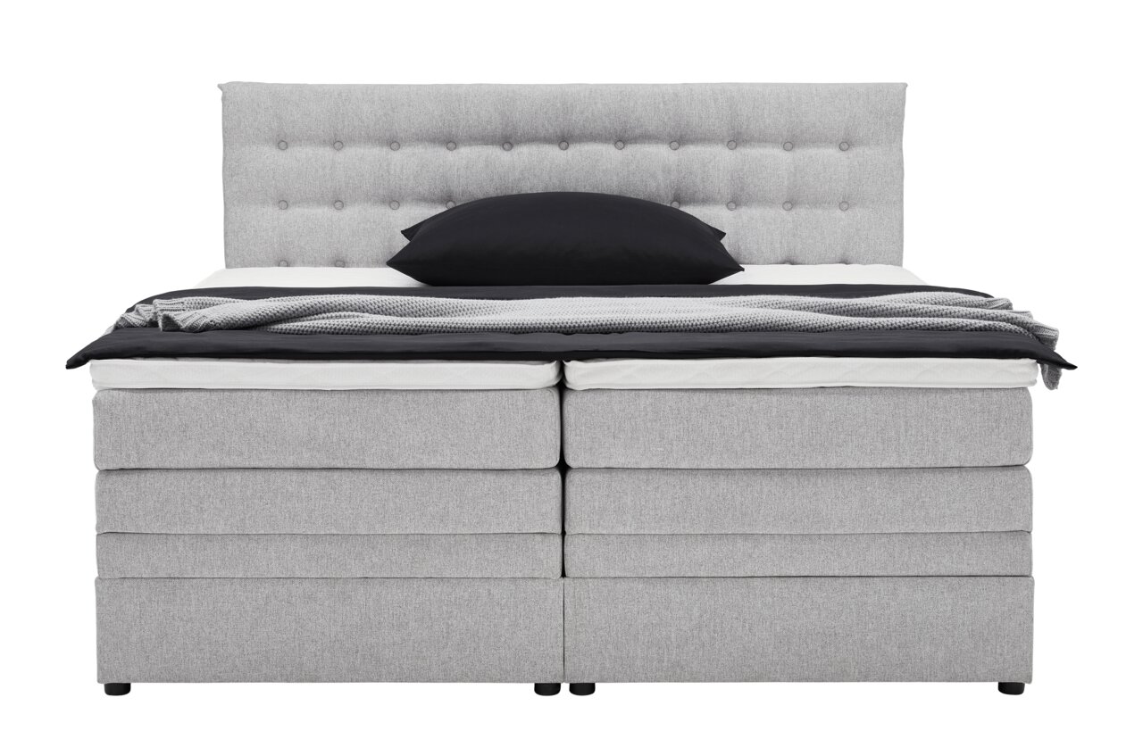 Frontale Ansicht eines grauen Boxspringbetts mit gepolstertem Kopfteil und schwarzem Kissen.