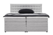 Frontale Ansicht eines grauen Boxspringbetts mit gepolstertem Kopfteil und schwarzem Kissen.