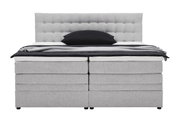 Frontale Ansicht eines grauen Boxspringbetts mit gepolstertem Kopfteil und schwarzem Kissen.