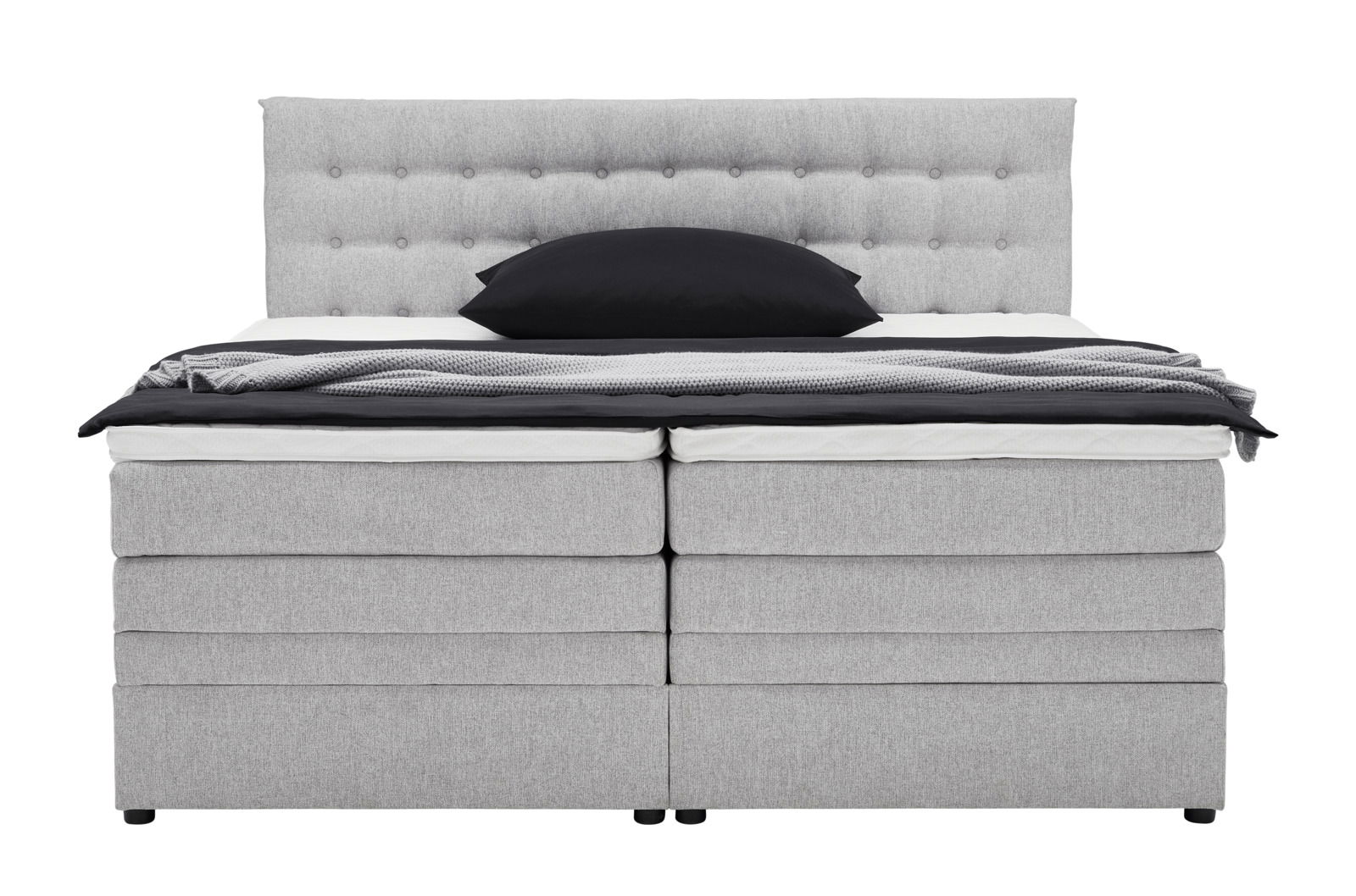 Frontale Ansicht eines grauen Boxspringbetts mit gepolstertem Kopfteil und schwarzem Kissen.