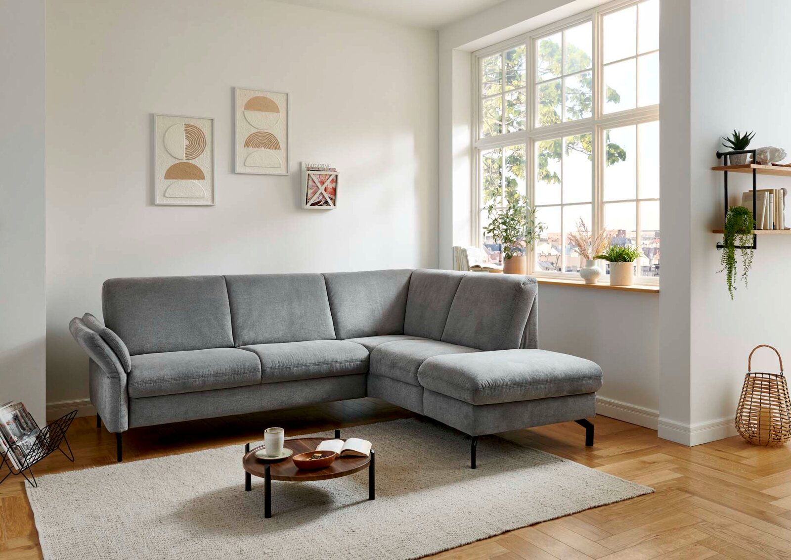 Graues Ecksofa in modernem Wohnzimmer, seitliche Perspektive mit großem Fenster im Hintergrund.