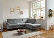 Graues Ecksofa in modernem Wohnzimmer, seitliche Perspektive mit großem Fenster im Hintergrund.