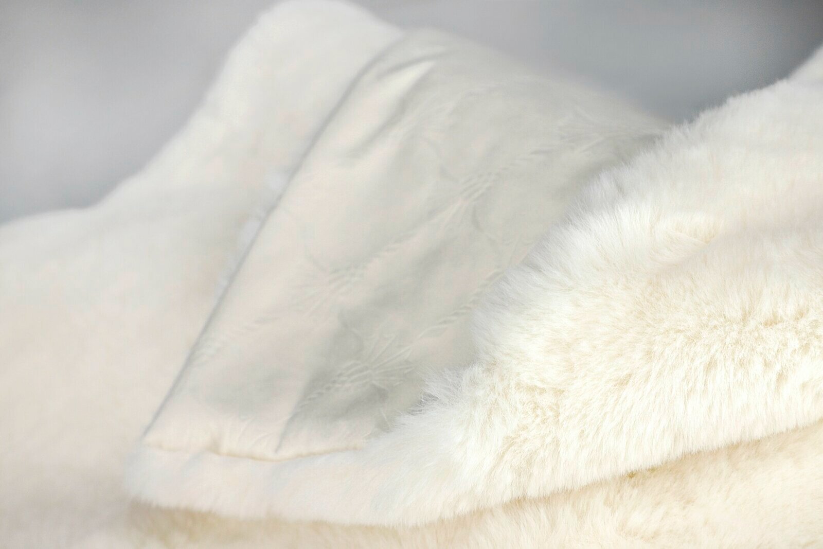 Nahaufnahme einer weichen, cremefarbenen Wohndecke mit flauschiger Textur und dezenter Musterung.