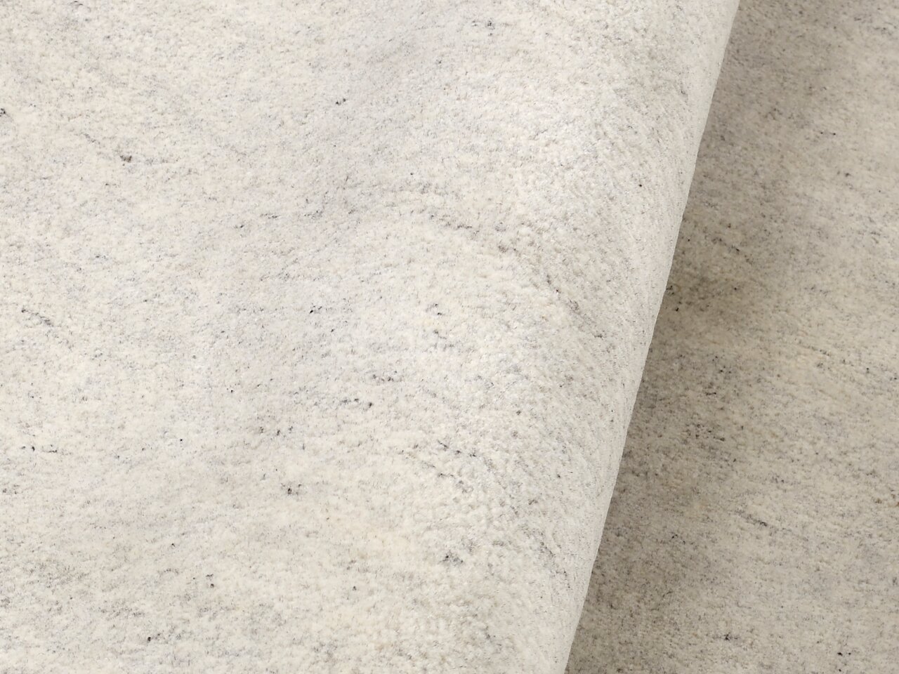 Nahaufnahme eines hellen Wollteppichs mit leicht melierter Textur, von der Seite betrachtet.