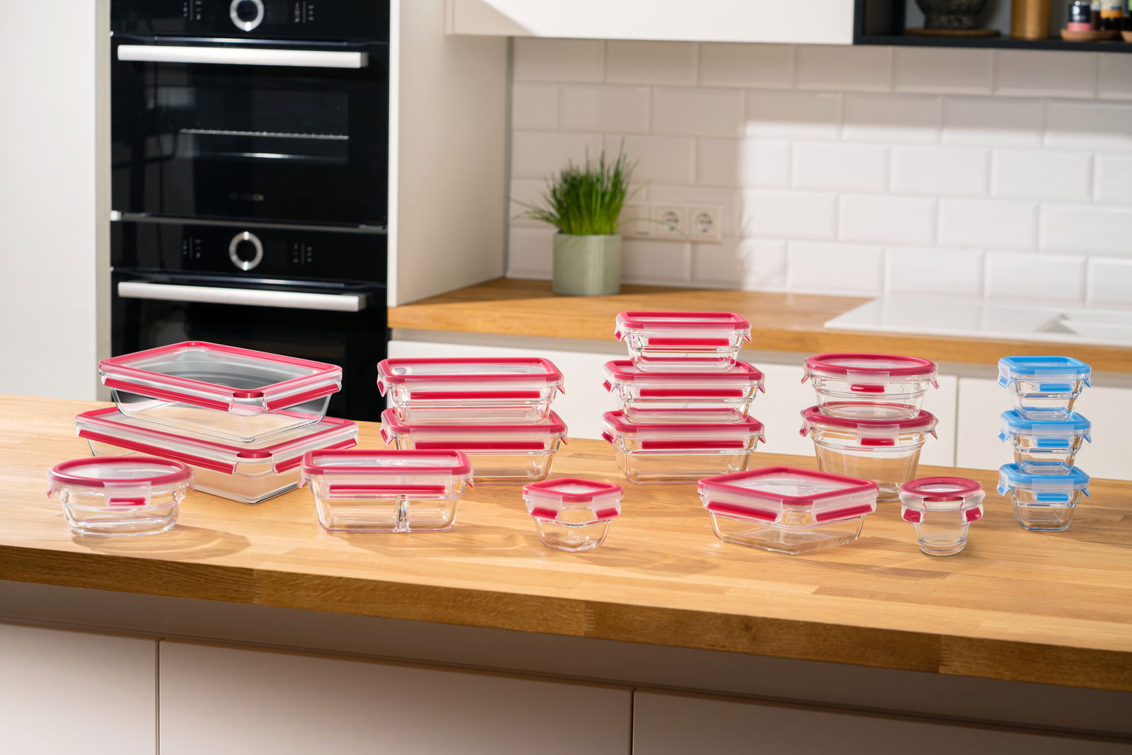 Verschiedene Glasbehälter mit bunten Deckeln auf einer Küchenarbeitsplatte, aus einer leicht erhöhten Perspektive fotografiert.