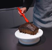 Roter Silikon-Backpinsel, der Schokolade auf einen Kuchen aufträgt, aus der Perspektive von oben.