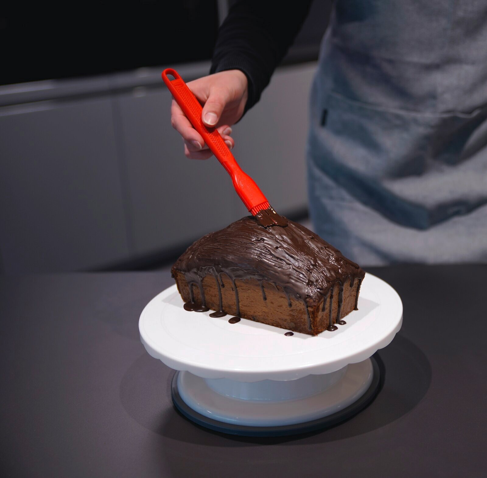 Roter Silikon-Backpinsel, der Schokolade auf einen Kuchen aufträgt, aus der Perspektive von oben.