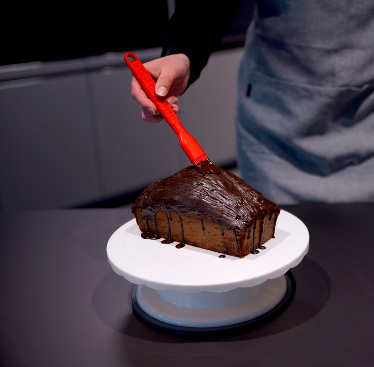 Een rode siliconen bakkwast die chocolade op een taart aanbrengt, gezien van bovenaf.