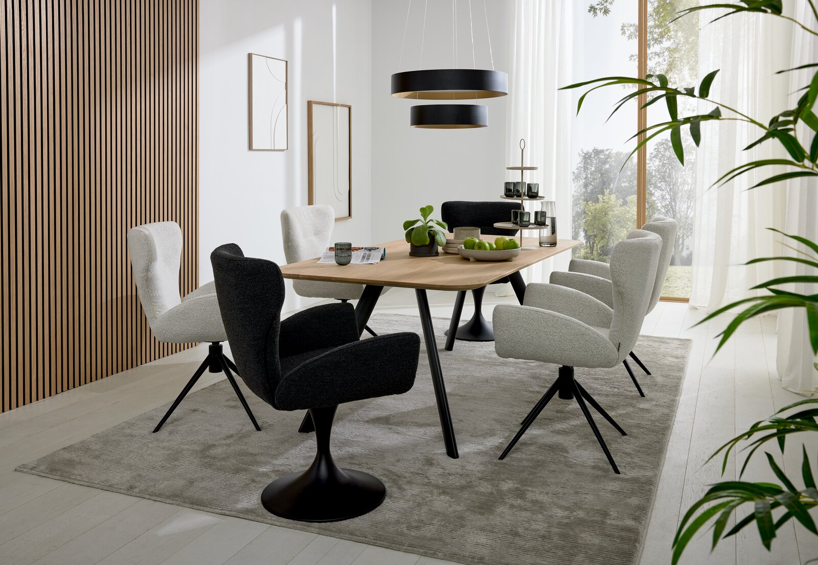 Musterring Esstisch MR JUSTB! Moderner Essbereich mit einem großen Holztisch und sechs gepolsterten Armlehnstühlen in einem hellen Raum mit großen Fenstern, seitliche Perspektive.