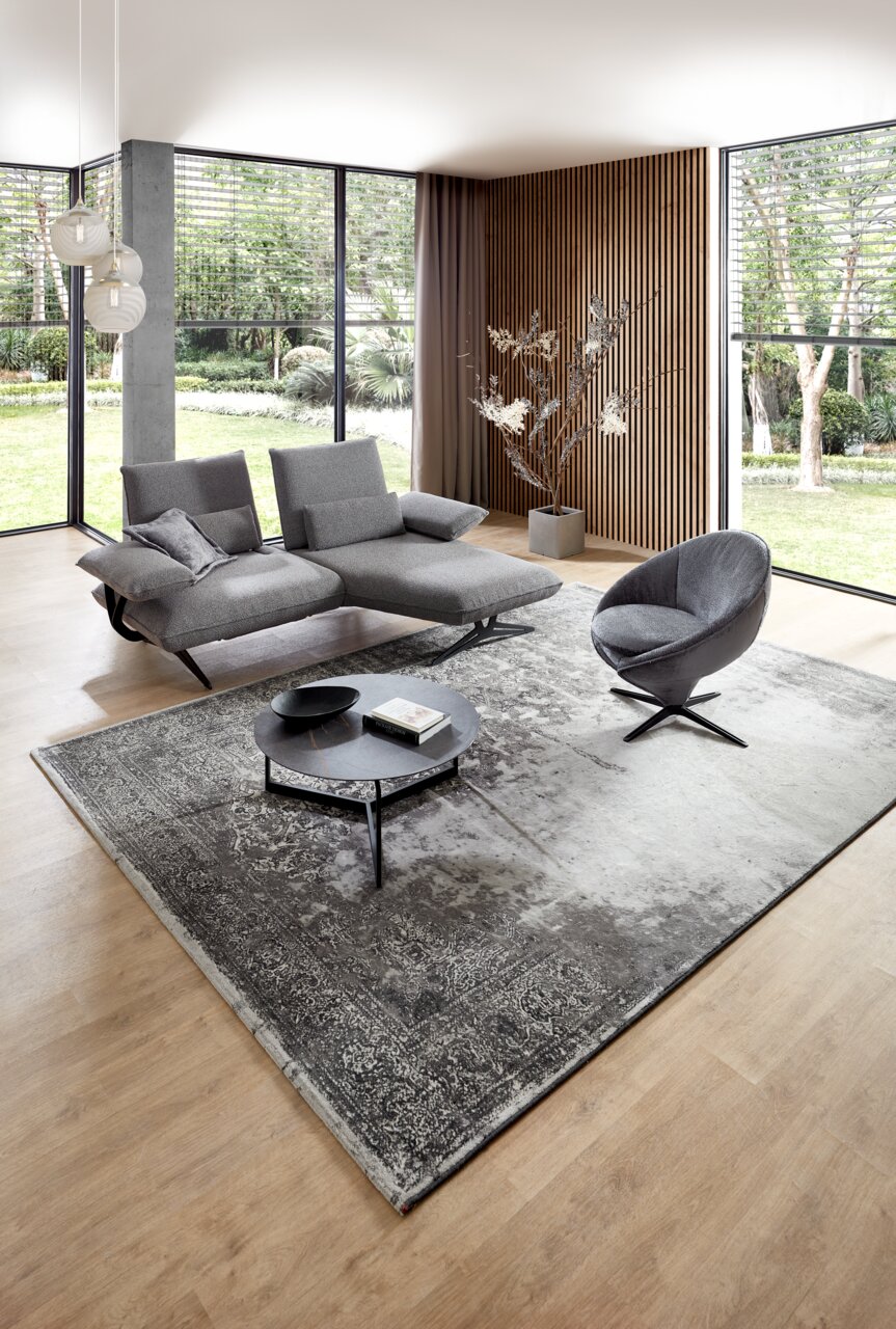 Koinor Sessel IMPULS Moderner grauer Sessel in einem stilvollen Wohnzimmer mit großen Fenstern und Holzwandverkleidung, seitliche Perspektive.