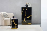 Moderner Beistelltisch in Schwarz mit goldenen Akzenten, frontal abgebildet neben einem cremefarbenen Sessel.
